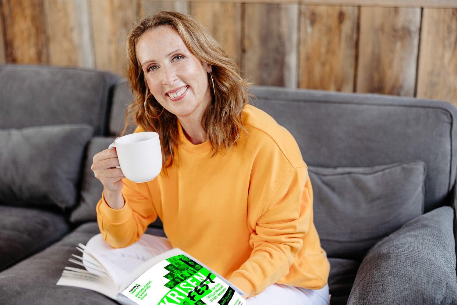 Annick auf dem Sofa mit Kaffee und dem Buch KRISENFEST